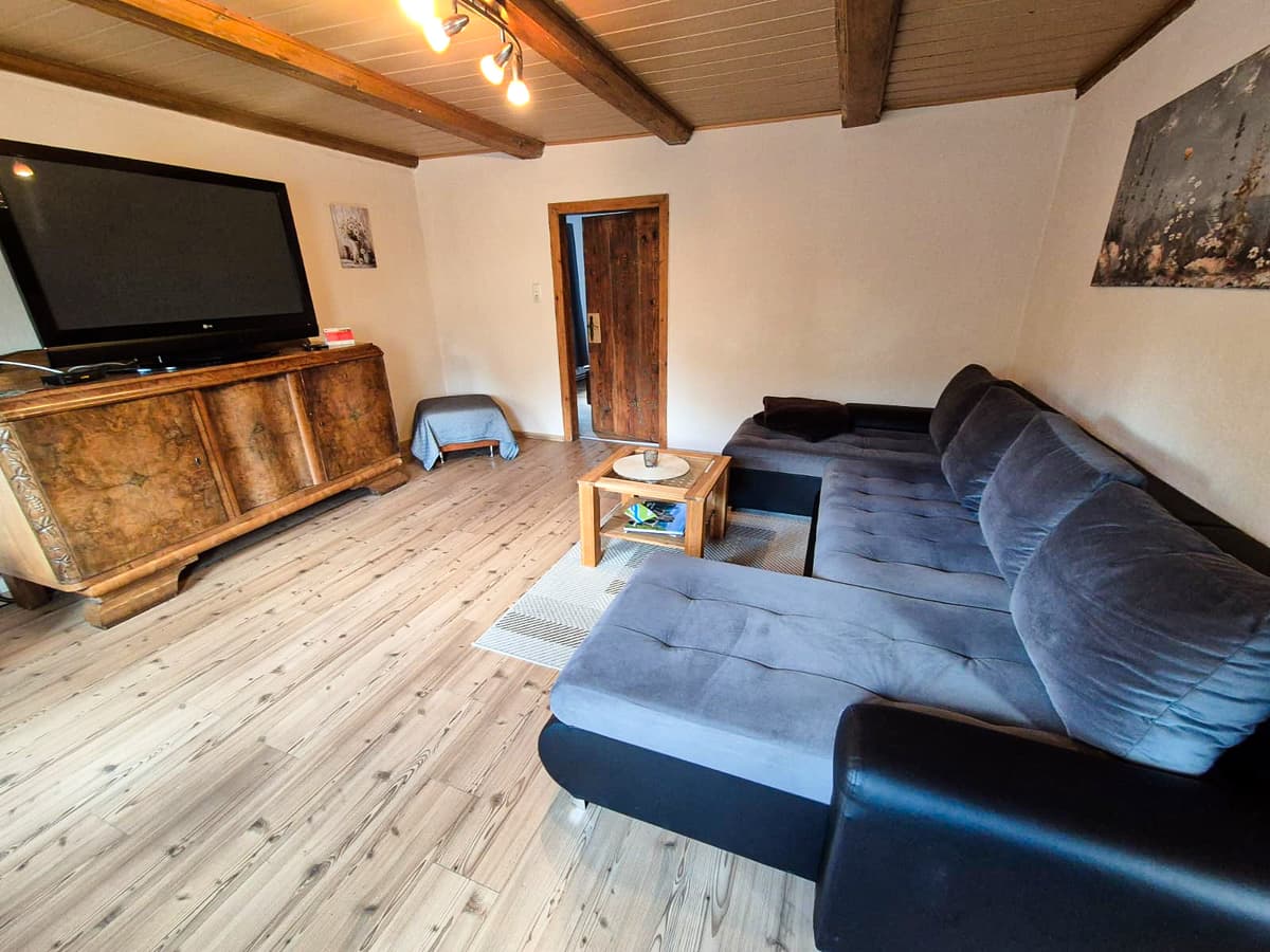 Wohnzimmer der großen Ferienwohnung mit großer Sitzgruppe, Fernseher und historischen Deckenbalken