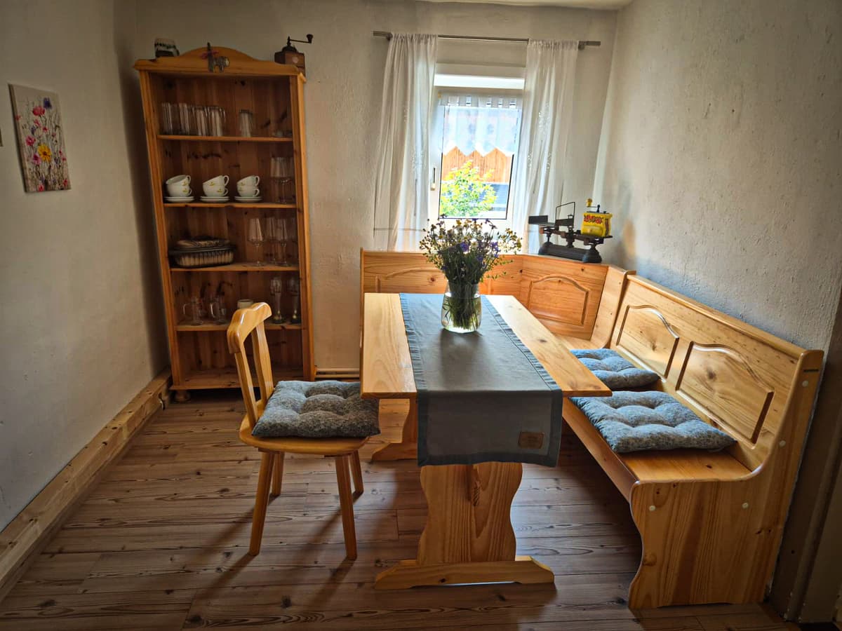 Esszimmer der kleinen Ferienwohnung mit Holztisch, Eckbank und Blumen