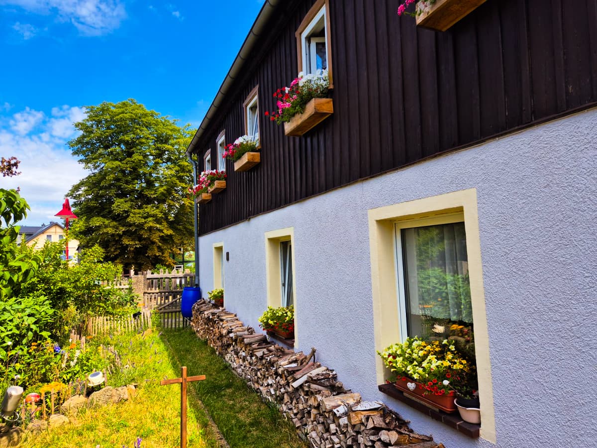 Kleiner Kuhstall mit dunkler Holzfassade, Blumenkästen und Garten